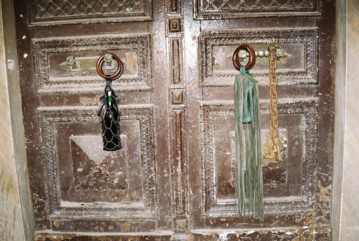 Asma and Üzüm wine bags hanging from the handles of an old wooden door